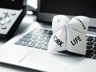 Piece of folded paper on top of a laptop, dived into sections, with the words, Work, Life & Balance
